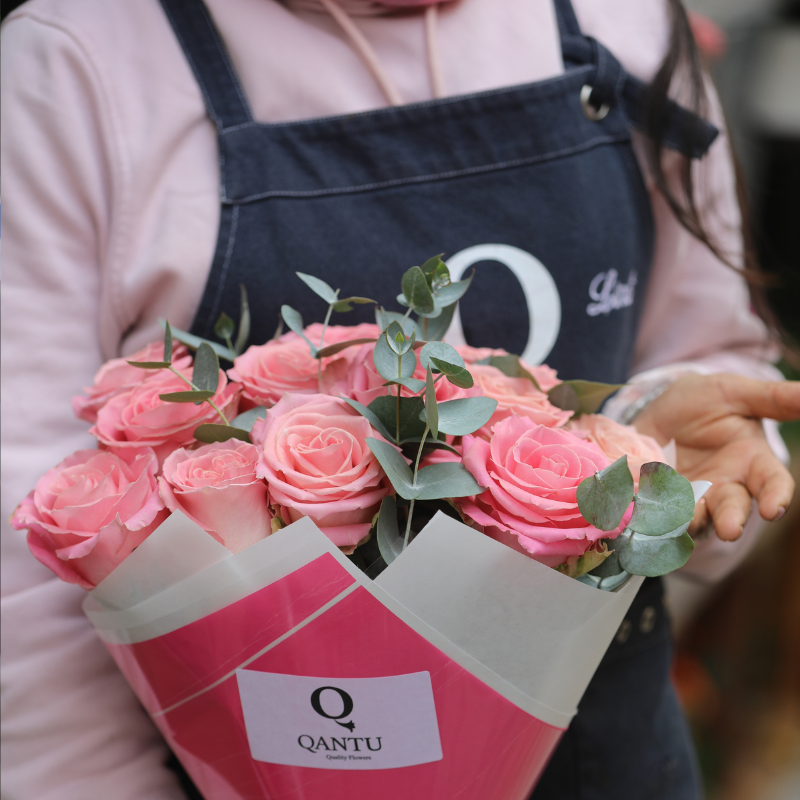 Florista de Qantu componiendo un ramo de rosas rosas y blancas con eucalipto sobre mesa de madera